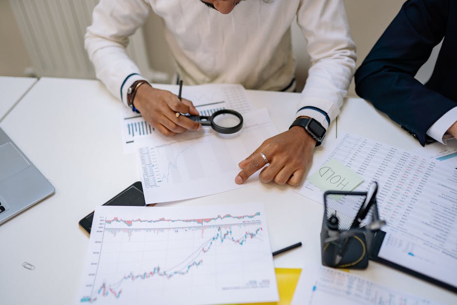 Business professionals reviewing charts with a magnifying glass in an office setting.